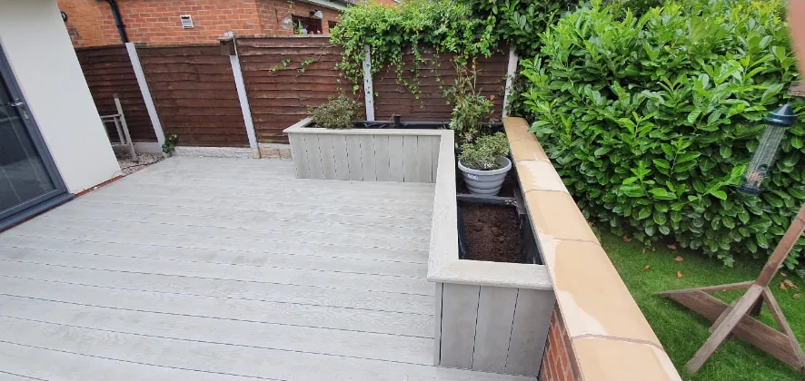 Grey composite decked area with rendered raised planters running alongside the lawn