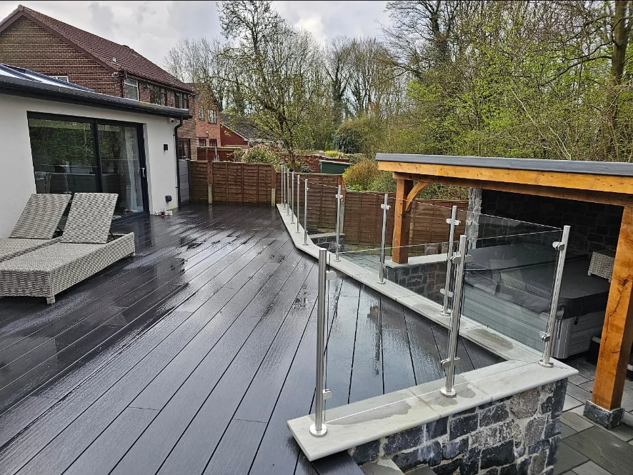 Dark composite decking with a stainless steel and glass balustrade overlooking a stone terrace