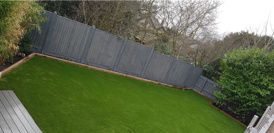 Rear garden lawn edged with timber, alongside grey painted close-board fencing