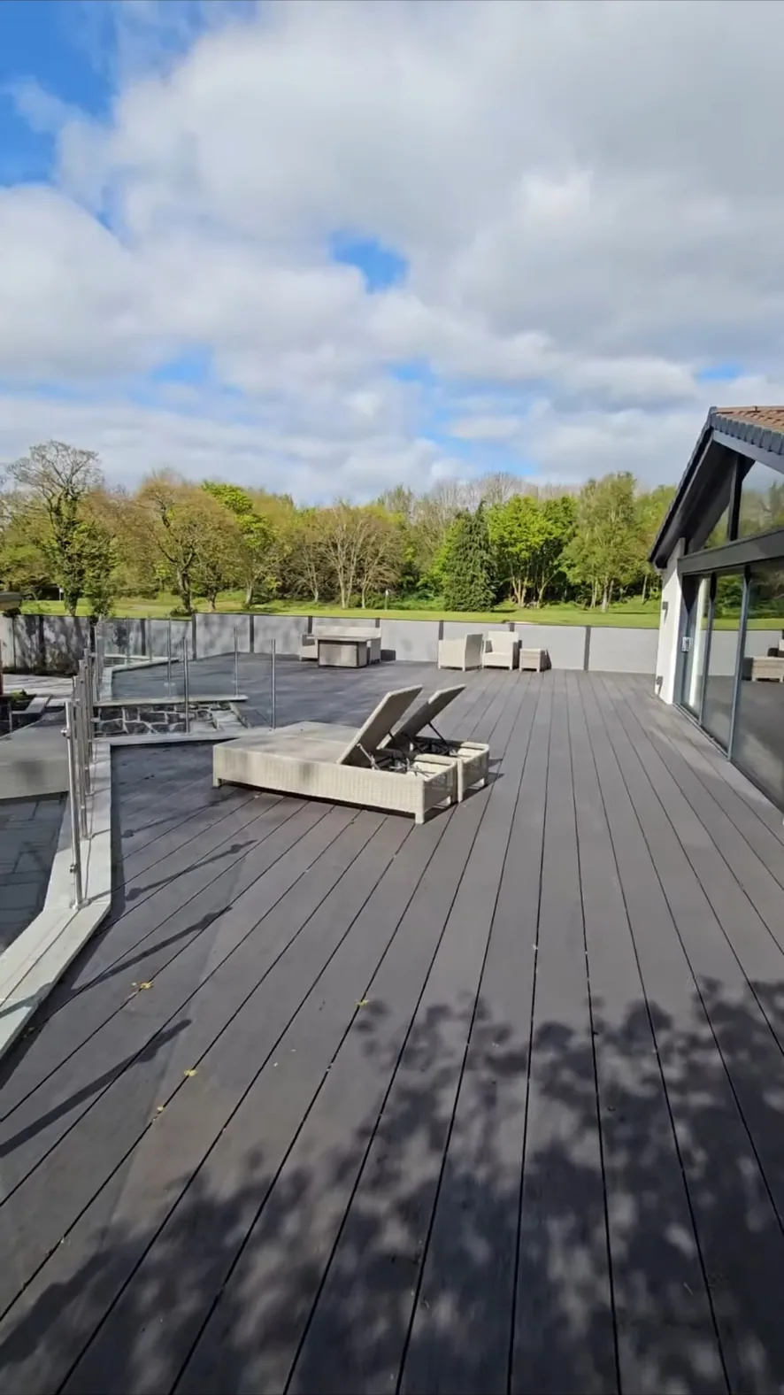 Wide view of the finished dark composite deck with a glass balustrade looking out over open parkland