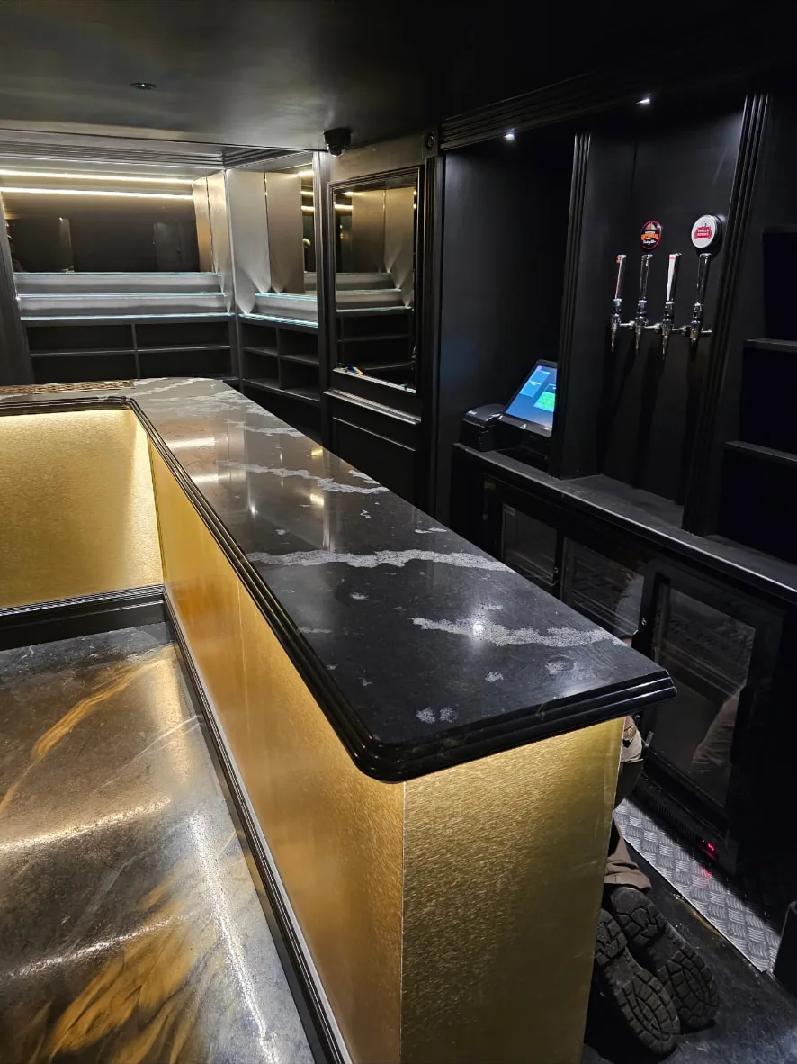 Servery run with gold panelling, moulded dark stone counter top and fitted beer taps behind