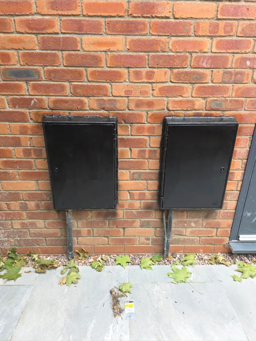 Two new black external meter boxes fitted to a red brick wall