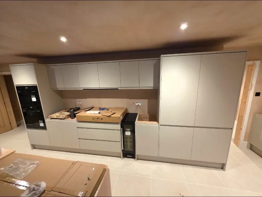 Handleless grey kitchen units with built-in double ovens and tall storage housings installed along a wall