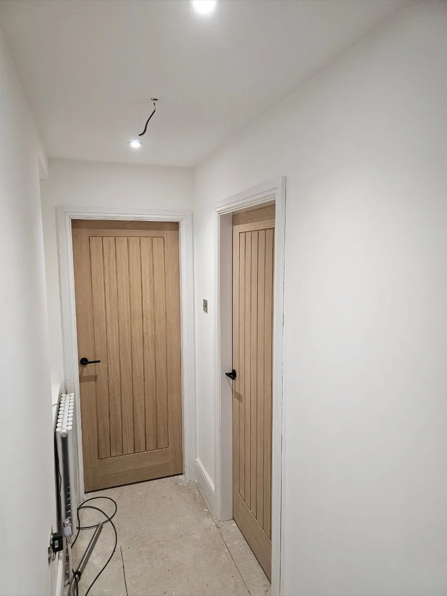 Two cottage-style oak internal doors hung with white architrave and black lever handles in a hallway